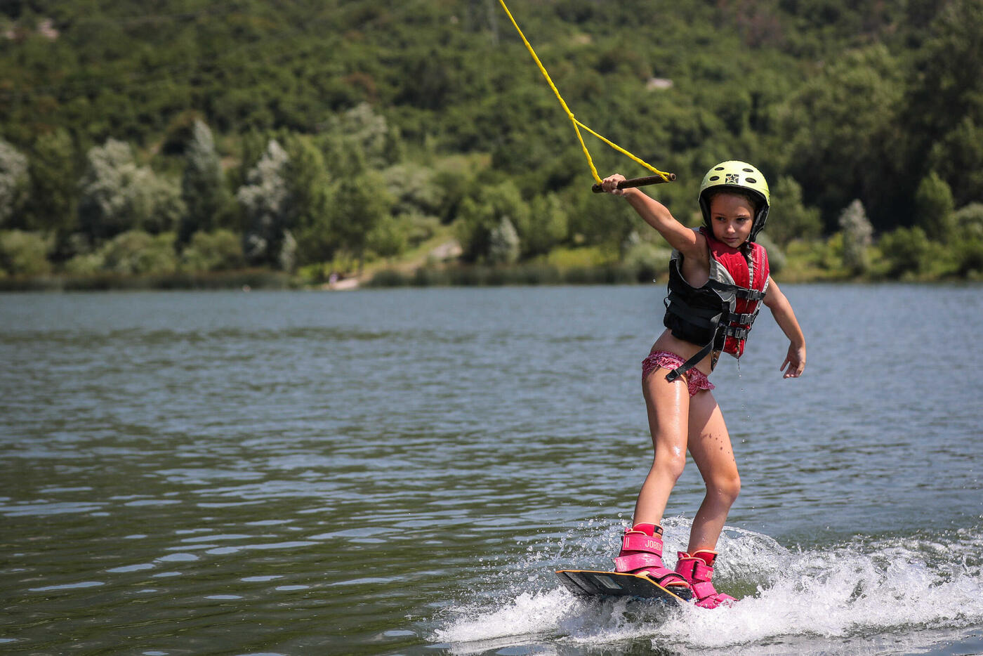 Una bambina con casco e giubbotto in piedi sulla tavola, trainata dal cavo