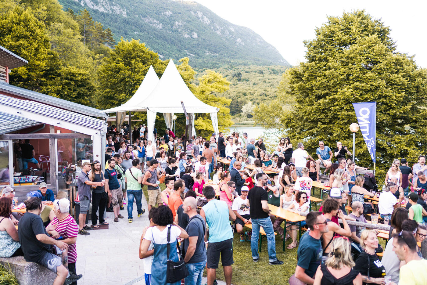 Il bar pieno di gente fra le tavolate e i gazebo bianchi, con il lago dietro